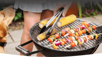 Grill mit Gemüse, im Hintergrund ist eine Frau mit einem Hund zu erahnen