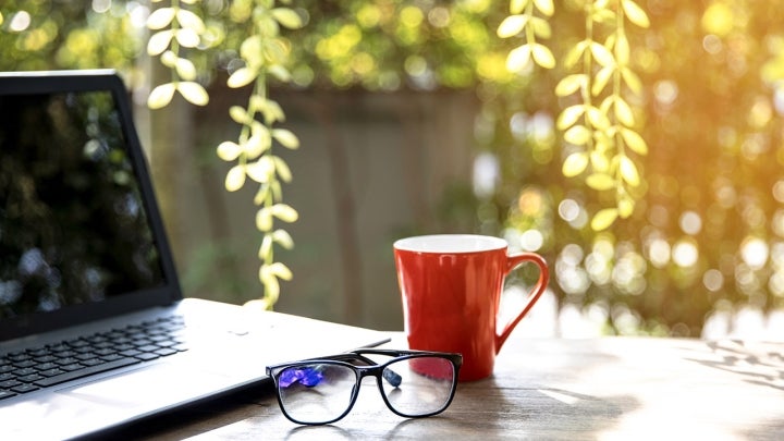 Laptop, Tasse und Brille auf einem Tisch