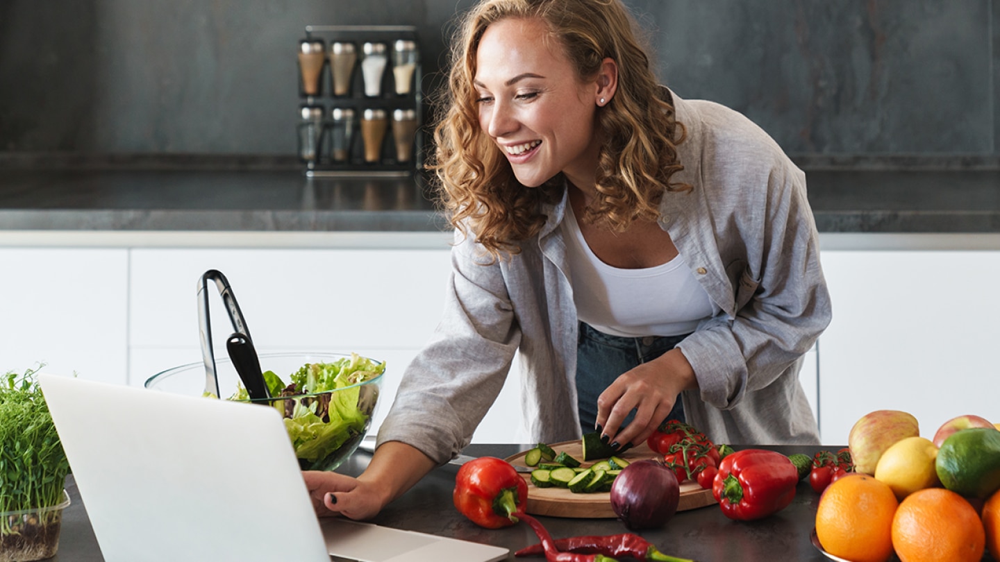 Junge Frau nutzt ihren Upfit-Ernährungsplan kostenlos auf einem Laptop beim Kochen