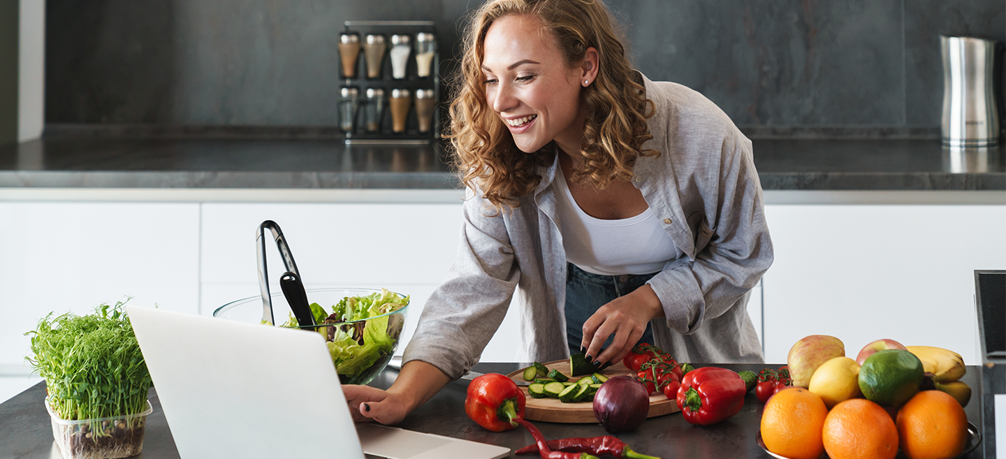 Junge Frau nutzt ihren Upfit-Ernährungsplan kostenlos auf einem Laptop beim Kochen